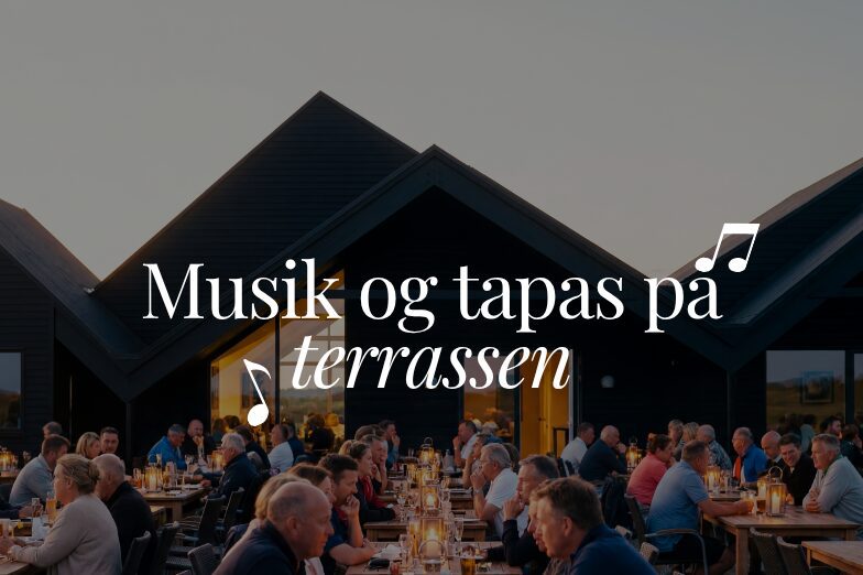 Gæster nyder tapas og levende musik på en stemningsfuld terrasse foran mørke træbygninger.